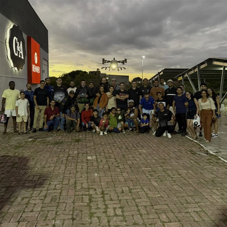 Turma numerosa reunida ao entardecer com um drone agrícola em voo